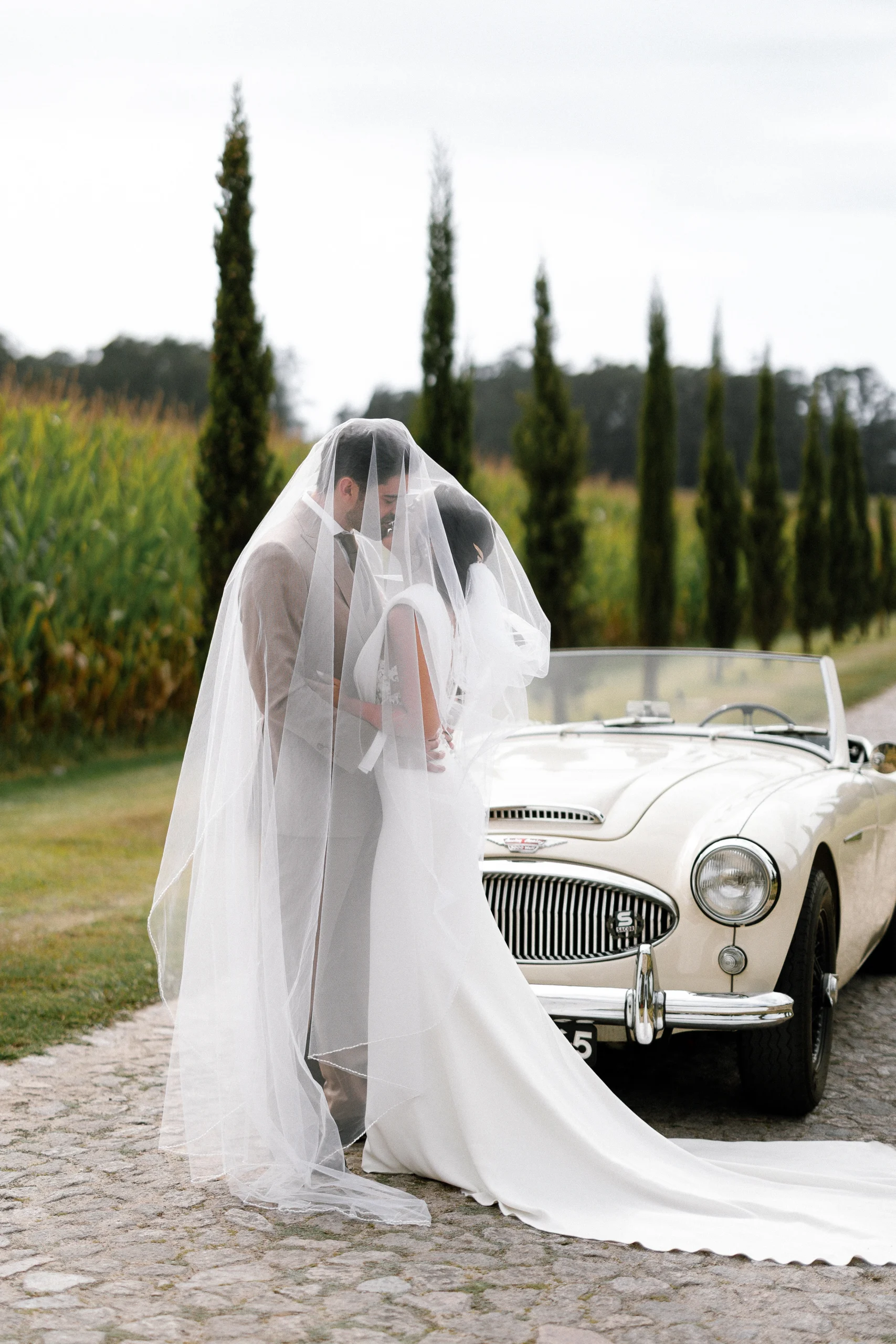 Bride and groom sharing an intimate moment beside a vintage car in Portugal